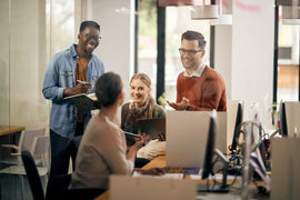 Four middle-aged people sitting in an office, smilling at each other. One is wearing his hearing aids in the workplace.