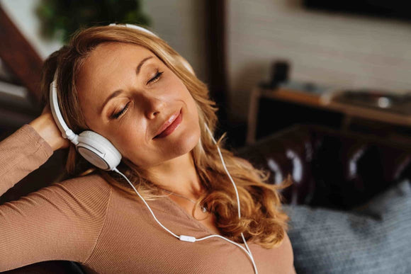 Blond, middle-aged woman sitting on the couch with her eyes closed wearing her headphones listening to loud music.