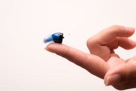 Go hearing aid resting on a woman's fingertip as she is about to care for her hearing aids.