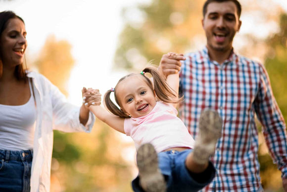 Smilling middle-aged man and woman swinging a laughing little girl between then by her hands.